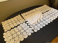 Nine handmade crochet placemats displayed on a dark oval table, showing the variety of patterns and scalloped edges.