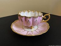 Front and side view of pink footed tea cup on matching saucer showing scalloped edge and gold gild accents.