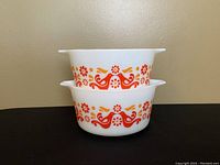 Two stacked Pyrex casserole dishes showing the side floral and ribbon pattern on white milk glass.