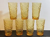 Front view of seven vintage amber crinkle drinking glasses arranged in two rows showcasing texture and color.