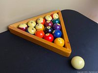 Top-down view of billiard balls numbered 1 to 15 arranged in wooden rack, with cue ball on black surface.