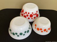 Three vintage Federal Glass mixing bowls upside down showing red, green, and orange polka dot patterns on opaque white glass.