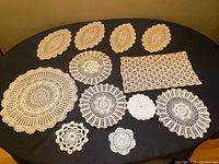 Overview of all 11 handmade crochet doilies laid out on a dark surface showing variety in shapes and sizes.