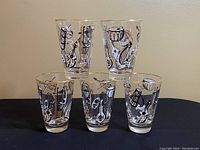 Front view of 5 vintage Libbey glasses with musical instrument designs and gold rims arranged in pyramid shape
