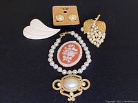 Overview of the vintage jewelry set including earrings, cameo brooch, pearl bead bracelets, and gold-tone pearl cluster brooch displayed on black fabric.