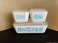 Set of four vintage Pyrex refrigerator dishes stacked showing the turquoise Butterprint pattern and clear glass lids.