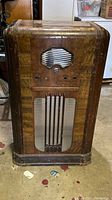 Front view of the antique wooden floor radio cabinet shell showing the grille, control holes, and wear on the exterior.