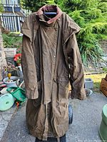 Full front view of the long brown Australian Outback jacket hanging showing length and snap buttons