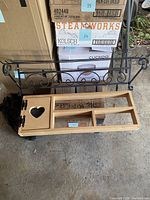 Metal coat rack with hooks and scroll design behind wooden hanging shelf with multiple compartments and heart cutout door