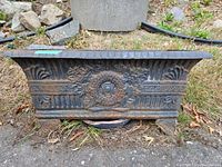 Front full view of the rectangular heavy iron planter highlighting overall shape, size, and decorative motifs including central wreath and fluted columns.