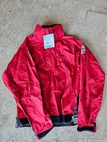 Front view of new red kayak jacket with tag attached, lying flat showing full zipper and collar.