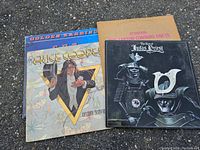 Four vinyl records stacked showing cover art and titles of Alice Cooper, Judas Priest, and Golden Earring albums.