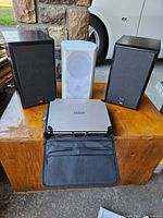 Two JBL 500 speakers, one white RCA portable DVD player (model DRC628), and a black carrying case displayed on wood surface.