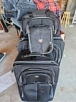 Photo showing stacked set of five black Swiss Gear luggage pieces in a garage setting.