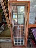 Full view of tall, narrow lead glass window with weathered wooden frame and visible brass handle on the side.