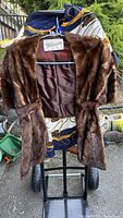 Full view of the brown mink fur stole hung for display showing the satin lining and belt.