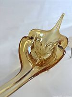 Amber stretch art glass sculpture with pointed tip and flowing organic curves, elevated on four clear glass feet.