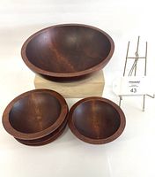 Top-down view of 1 large round wooden salad bowl and 4 smaller wooden bowls stacked beside it showing shape and wood grain