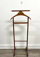 Full wood suit valet stand showing hanger, pants bar, and brass footrest base.