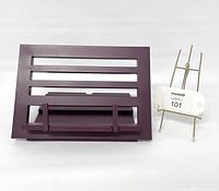 Front view of aubergine metal book stand with horizontal slots, front ledge, and support frame next to small metal easel.