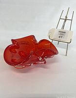 Side view of the deep red glass ashtray showing the free form shape and smooth glass finish.