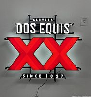 Front view of the Dos Equis LED neon sign illuminated on a wall, showing white text and large red double X logo.