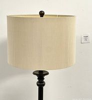 Close-up of beige pleated fabric lamp shade with damage inside and dark finial at top