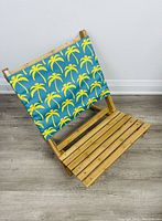 Front view of the bamboo chair with blue fabric backrest printed with yellow palm trees, showing slatted bamboo seat and frame against a white wall background.