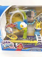 Front view of toy packaging showing parakeet toy perched on green stand with play accessories inside clear plastic box.