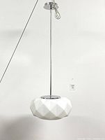 Full view of ceiling light showing long chrome pole and white geometric faceted shade hanging downward.