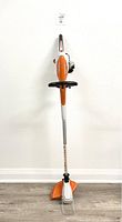 Front view of the Stihl FSA 45 battery trimmer showing its full length with orange-white design and black safety guard at cutting head.