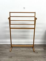 Front view of teak blanket rack standing upright showing four horizontal bars and stable base feet.