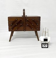 Full view of vintage wooden accordion sewing box with legs and handle, showing front expansion arms and general condition