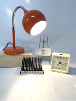 Photo of the red gooseneck desk lamp, black coil letter holder, and beige Allegro alarm clock arranged together on a surface.