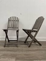 Two vintage wooden folding chairs, one facing forward and one at an angle showing side profile.