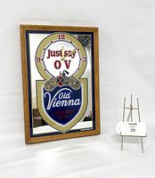 Full view of the vintage mirrored Old Vienna beer bar clock with oak frame, standing upright with a small easel next to it for scale.