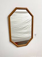 Full view of the oak framed elongated octagon mirror hanging on a white wall.