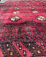 Close-up angle showing deep red wool pile with repeating geometric floral motifs and intricate handmade border