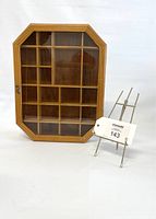 Front view of vintage wooden curio cabinet with glass front and magnetic clasp, showing multiple interior sections. A small display easel is beside it for scale and item tag.