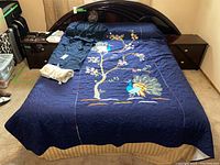 Full bed showing navy blue quilt with peacock and floral embroidery, black robe and heating pad on bed