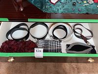 Drawer showing five men's belts in black, white, and brown, assorted ties and scarves underneath
