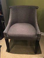 Front view of the grey upholstered armchair showing the curved back and nailhead trim.