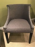 Front view of gray upholstered accent chair with nailhead trim and dark wooden legs.