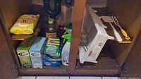Cleaning supplies under kitchen cabinet, showing sponges, trash bags, and spray bottles.