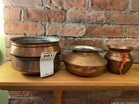Three copper urns with distinct shapes and one with orange string