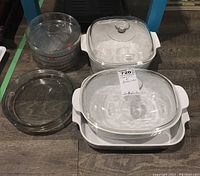 Corning bakeware dishes with lids and four round glass pie plates stacked.