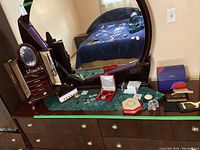 Wide view of wooden dresser top with costume jewelry, jewelry boxes, wallets, and jewelry box with mirror reflecting room.
