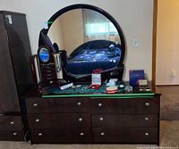 Front view of the dresser with round mirror mounted and various small items on top, showing laminate finish and chrome drawer knobs.