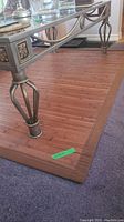 Area rug shown under a table with metal legs; wooden plank design with brown fabric border, tag labeled 'MAX' visible on corner.