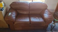 Front view of brown leather loveseat showing two seating areas with cushioned back and arm rests.